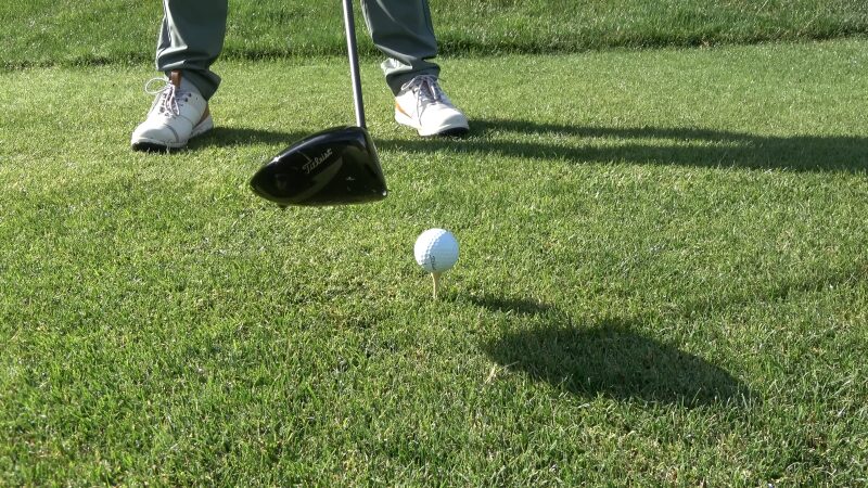 A Golfer Prepares to Swing with A Driver, with A White Golf Ball Placed on A Tee