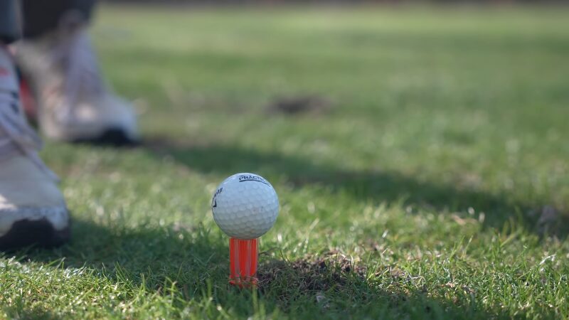 A White Golf Ball Is Placed on A Bright Orange Tee on A Grassy Course