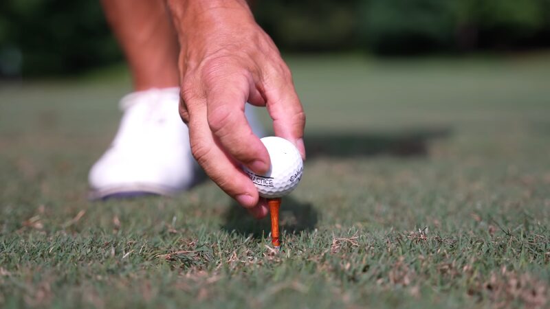 A Golfer Places a White Ball on An Orange Wooden Tee