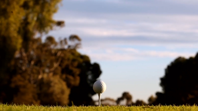 A White Golf Ball Sits on A White Tee Against a Scenic Backdrop