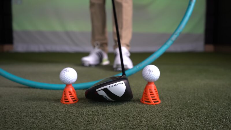 A Driver Is Positioned Behind Two Golf Balls Set on Orange Practice Tees